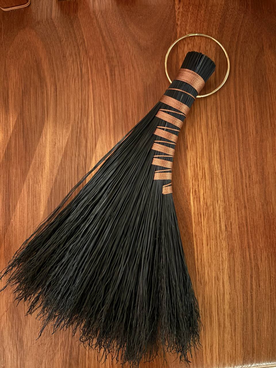 Black handmade broom with copper binding and a brass hanging ring.