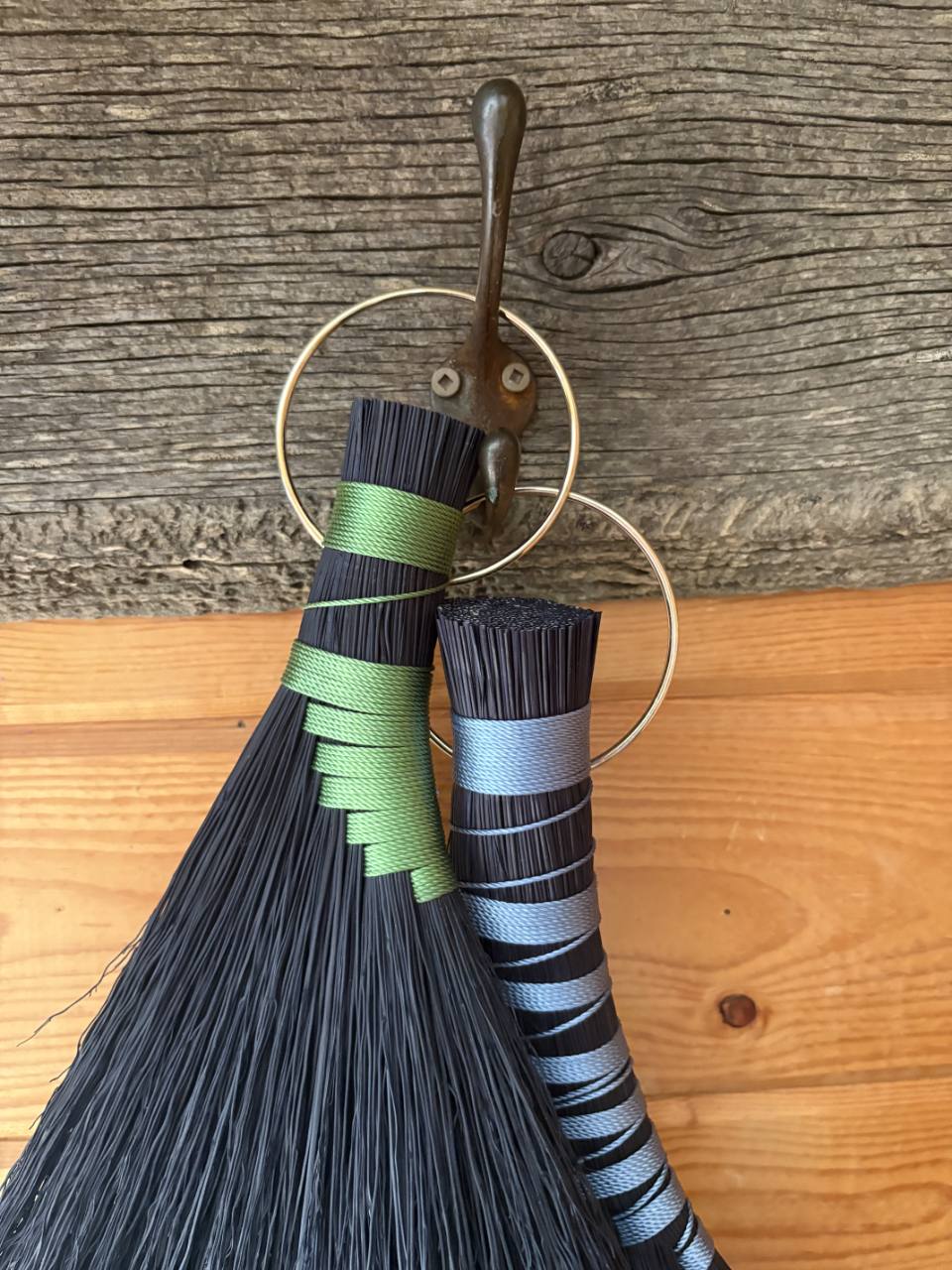 Close-up of black hand brooms with green and blue binding on brass rings.