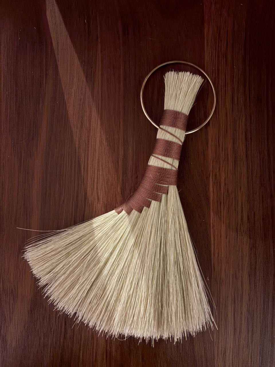 Fan-shaped natural hand broom with russet binding on a dark wood surface.